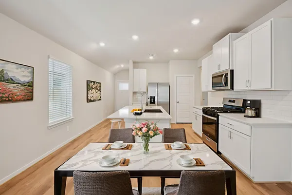 a kitchen with stainless steel appliances granite countertop a stove a sink a microwave a refrigerator white cabinets and wooden floor