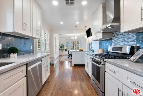 a kitchen with stainless steel appliances granite countertop a stove a sink dishwasher and a refrigerator with wooden floor