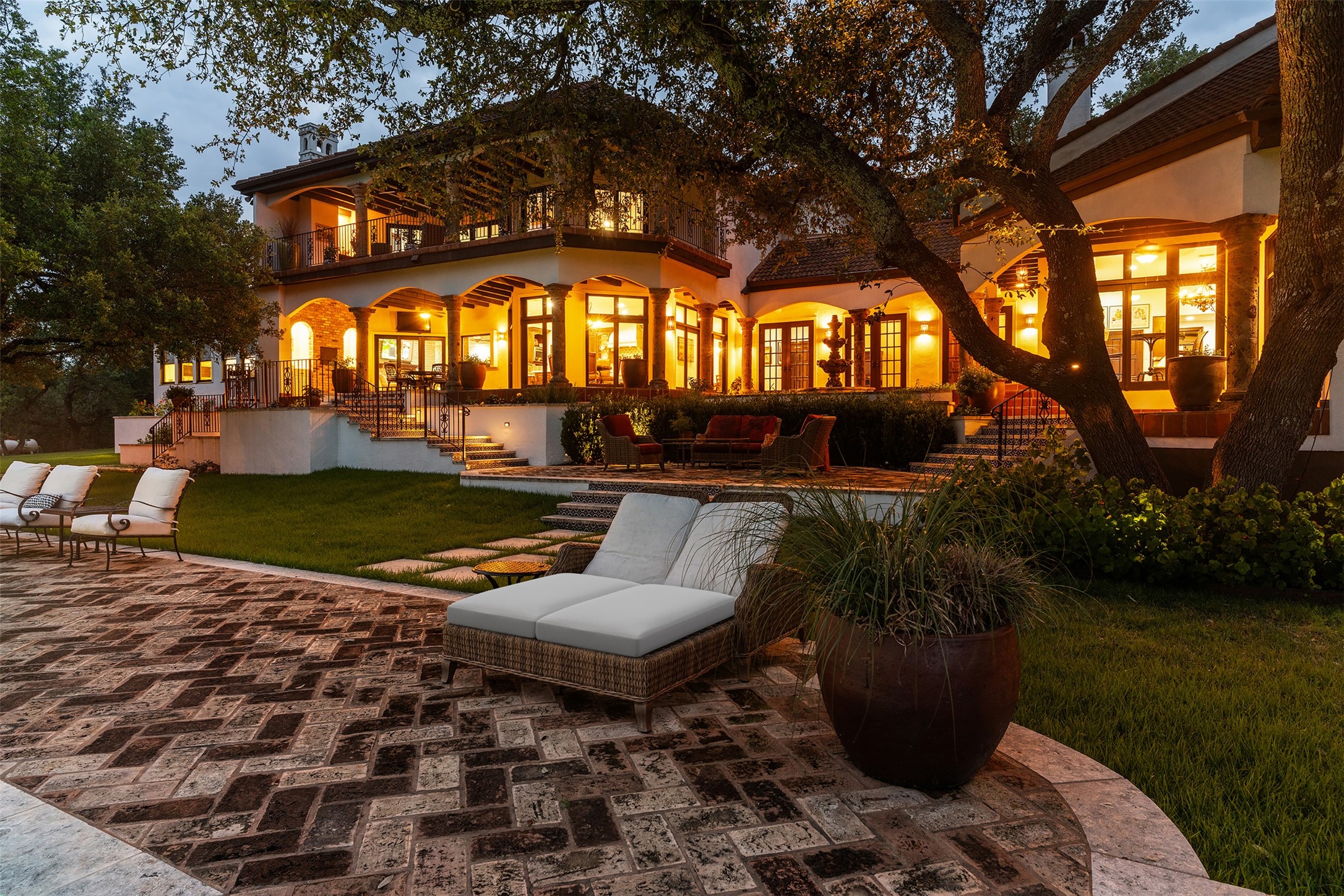 34000 Smithson Valley Road Bulverde, TX 78163 - Photo 36 of 50 The home's striking Mediterranean architecture is showcased by illuminated covered patios, cantera stone columns, and graceful outdoor living spaces. Warm evening lighting highlights the estate’s timeless elegance and resort-style ambiance.