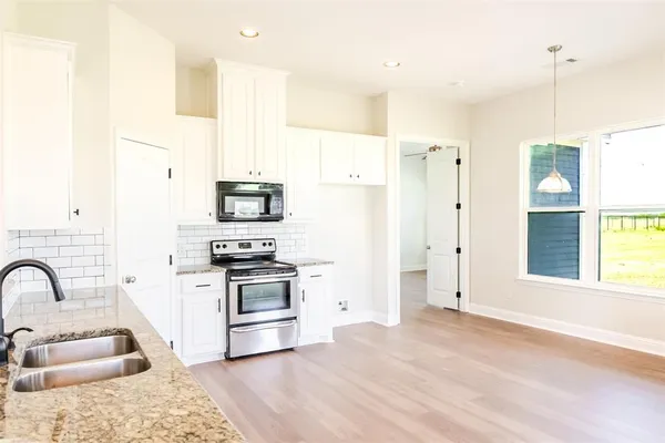 a kitchen with stainless steel appliances granite countertop a refrigerator a stove and a sink with wooden floors