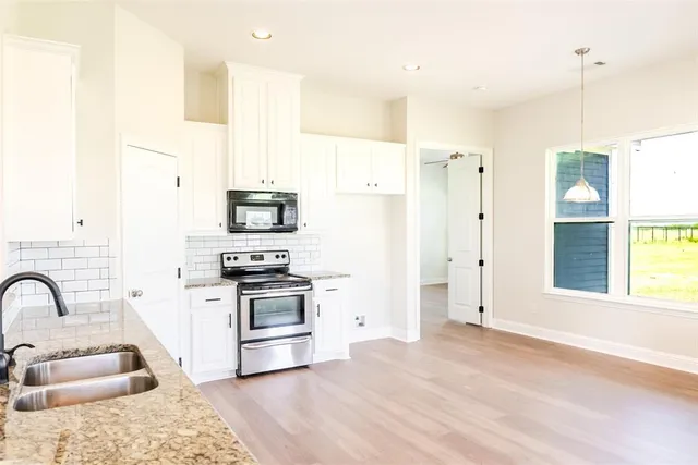 a kitchen with stainless steel appliances granite countertop a refrigerator a stove and a sink with wooden floors