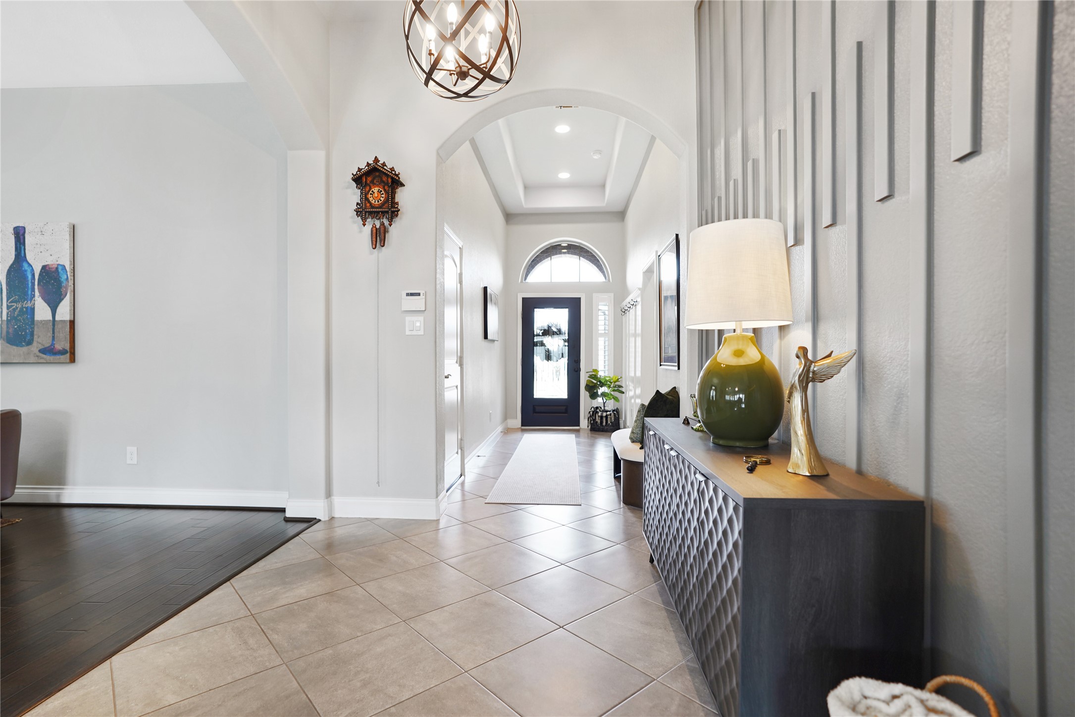 2345 Redwood Ridge Trail Manvel, TX 77578 - Photo 11 of 39 This photo shows a stylish, well-lit entryway with high ceilings and a modern light fixture. There's a decorative wall feature, a console table with a lamp and sculpture, and tile flooring leading to a dark front door with glass panels, offering a welcoming and elegant first impression.