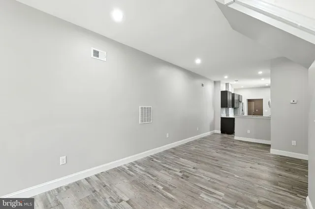 a view of an empty room with wooden floor and a kitchen