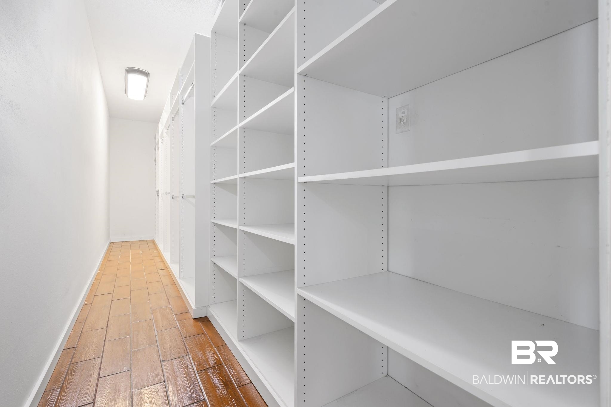 7540 2 Mile Road Irvington, AL 36544 - Photo 39 of 82 Hallway featuring built-in white shelving, wood-finish flooring, white walls, and a flush-mount ceiling light