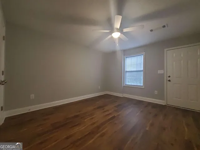 an empty room with wooden floor fan and windows