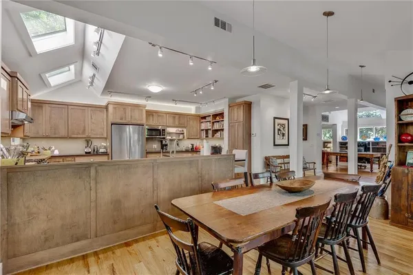 a kitchen with stainless steel appliances kitchen island granite countertop a dining table chairs and a refrigerator