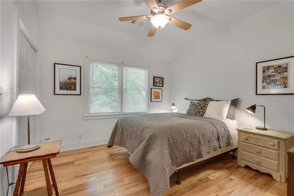 a bedroom with a bed and a lamp on dresser with wooden floor