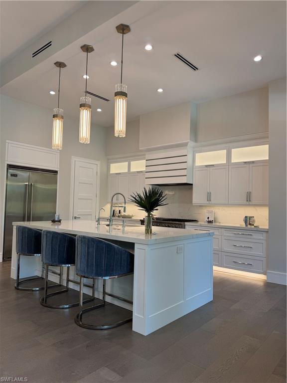 569 Neapolitan Way Naples, FL 34103 - Photo 11 of 50 Kitchen with visible vents, dark wood-type flooring, white cabinetry, fridge, and decorative backsplash