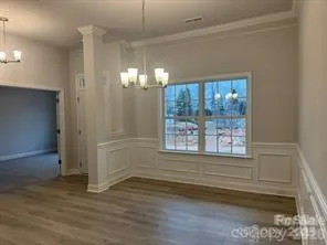 an empty room with wooden floor chandelier and windows