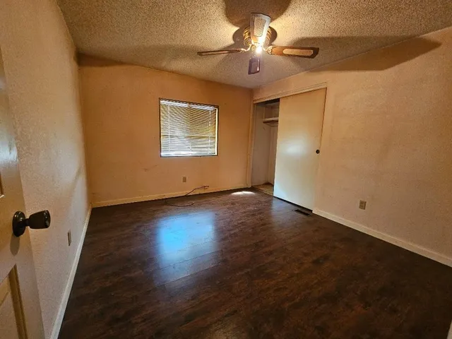 an empty room with wooden floor fan and windows