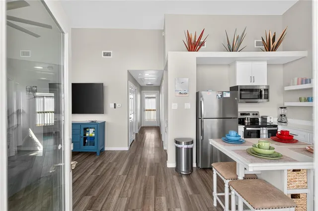 a living room with stainless steel appliances furniture a flat screen tv and a refrigerator