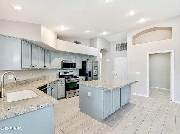 a kitchen with stainless steel appliances granite countertop a stove top oven a sink dishwasher and a refrigerator with wooden floor