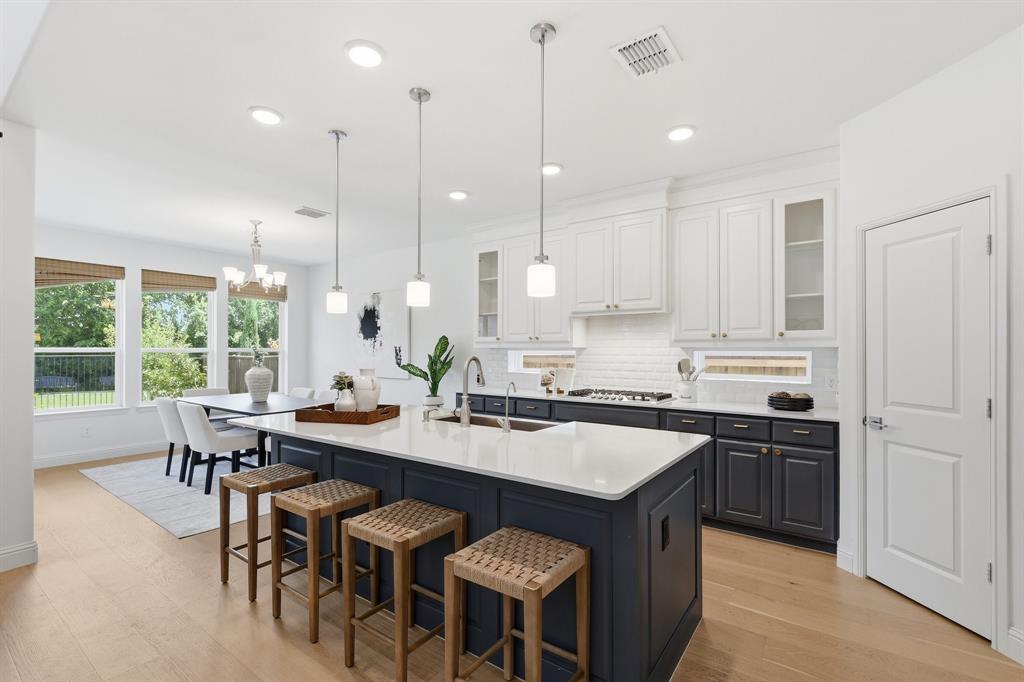 539 Farrell Lane Allen, TX 75013 - Photo 12 of 39 Open-concept kitchen featuring a large island with white stone-finish countertop, pendant lighting, two-tone cabinetry, and wood-finish flooring