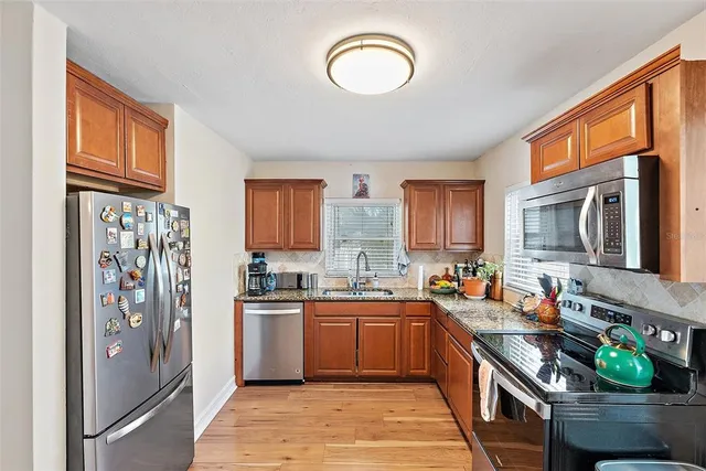 a kitchen with stainless steel appliances granite countertop a stove a sink dishwasher and a refrigerator with wooden cabinets