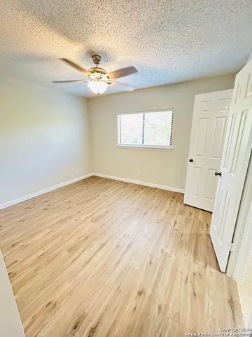 an empty room with wooden floor fan and windows