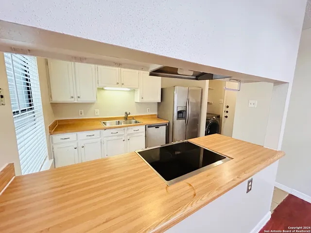 a kitchen with stainless steel appliances a stove a refrigerator a sink and white cabinets with wooden floor