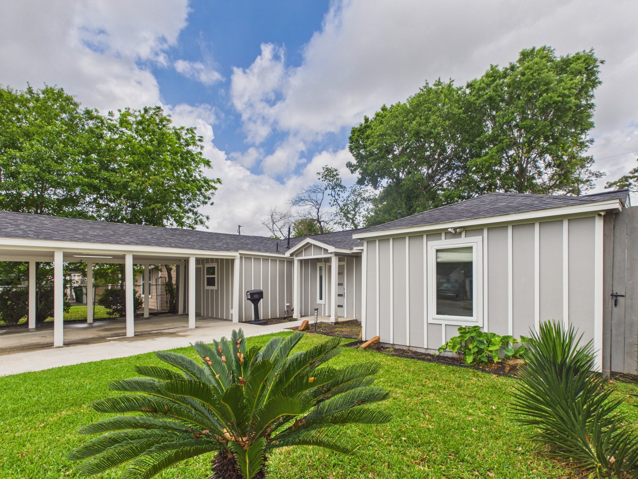 4927 Kelso Street Houston, TX 77021 - Photo 7 of 45 This charming home features a modern exterior with gray siding and white trim, complemented by a well-maintained front lawn and mature trees. The property includes a covered carport and a welcoming entryway, offering both functionality and curb appeal.