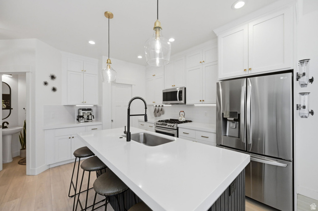 57 McCall Ln. Farmington, UT 84025 - Photo 7 of 36 Kitchen featuring a large island with an undermount sink and matte black faucet, white shaker-style cabinetry with brass-finish hardware, stainless steel appliances