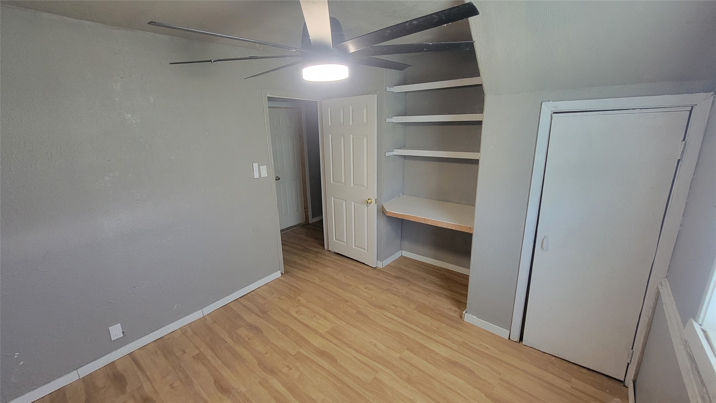 12018 Sandpiper Road Angleton, TX 77515 - Photo 23 of 48 This cozy room features laminate wood flooring, gray walls, a ceiling fan with light, built-in shelves, and a small closet. The door leads to a hallway, and a window allows natural light to brighten the space. Ideal for a small bedroom or office.
