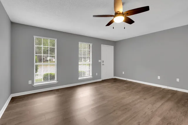 an empty room with wooden floor chandelier fan and windows