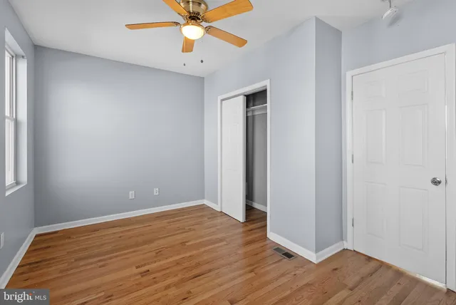 an empty room with wooden floor fan and windows