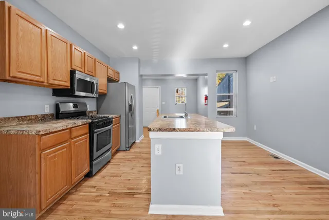 a kitchen with stainless steel appliances granite countertop a stove top oven a refrigerator a sink and dishwasher with wooden floor