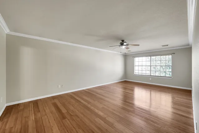 an empty room with wooden floor chandelier fan and windows