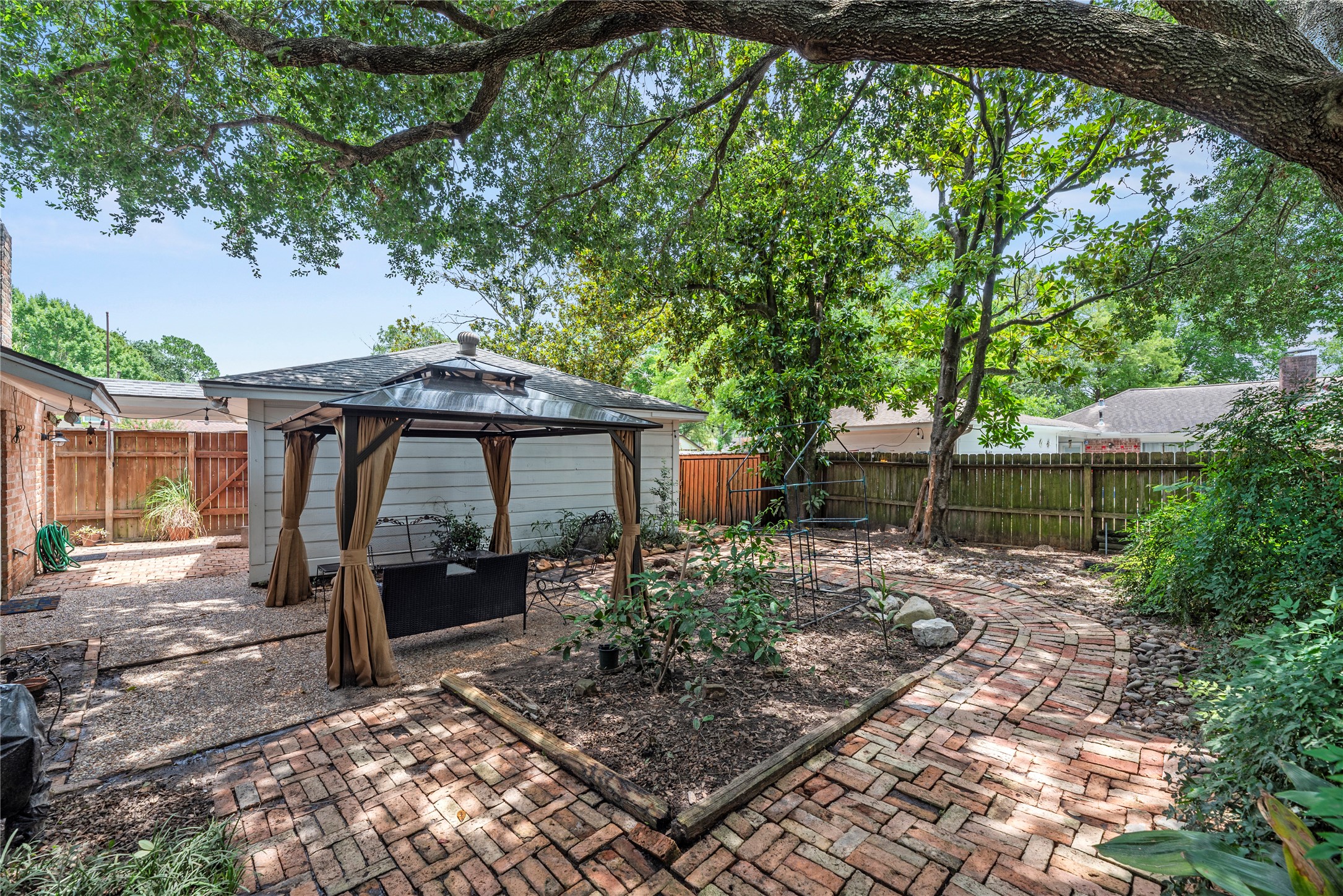 14203 Wickersham Lane Houston, TX 77077 - Photo 21 of 25 Alternate view of the backyard layout showcasing the circular brick-paved pathways, landscaping beds, and a fully fenced perimeter providing excellent privacy.