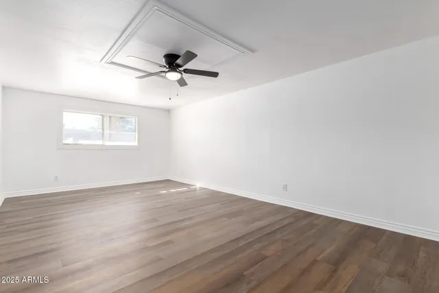 a view of an empty room with wooden floor and a ceiling fan