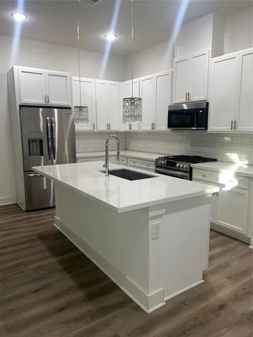 a kitchen with stainless steel appliances granite countertop a sink a stove a refrigerator and island with wooden floors