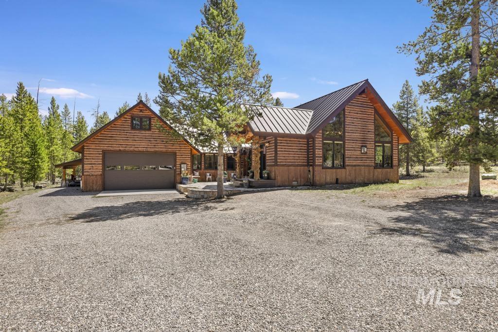 Log cabin style home featuring a metal roof, prominent A-frame window design, an attached garage with a frosted panel door, and a spacious gravel driveway