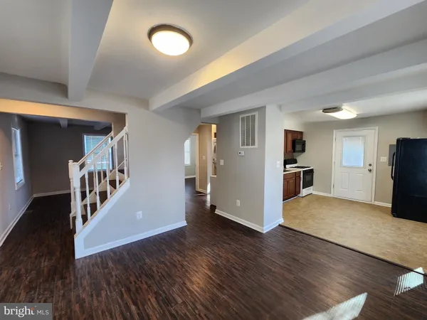 a view of an empty room with wooden floor and a kitchen