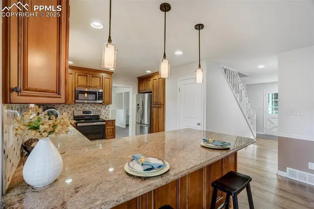 a kitchen with stainless steel appliances granite countertop a refrigerator a stove a sink and chairs