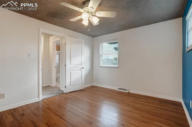 an empty room with wooden floor fan and windows