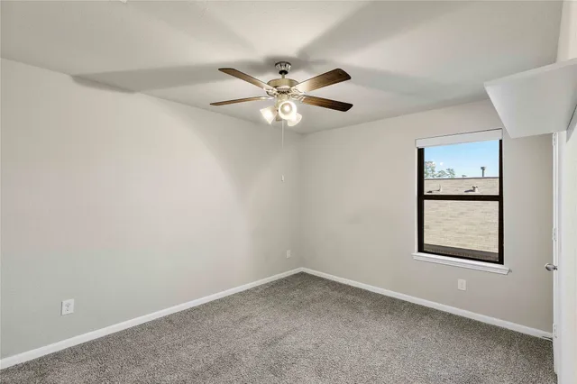 an empty room with chandelier fan and windows
