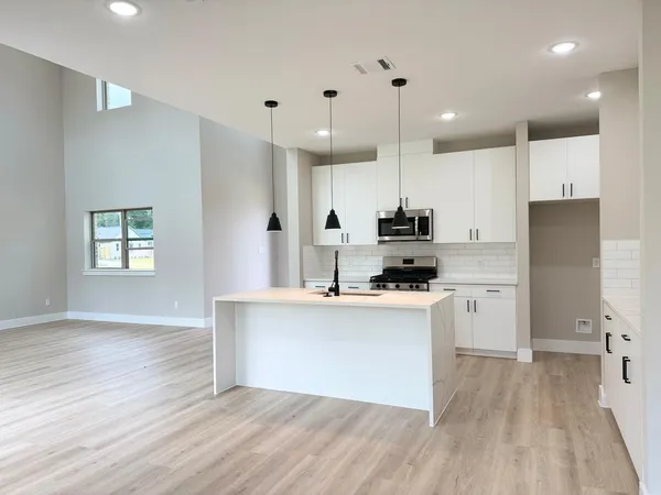 a large kitchen with a large counter top a sink stainless steel appliances and cabinets