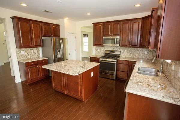 a kitchen with stainless steel appliances granite countertop wooden cabinets a sink dishwasher a stove and a refrigerator with wooden floor