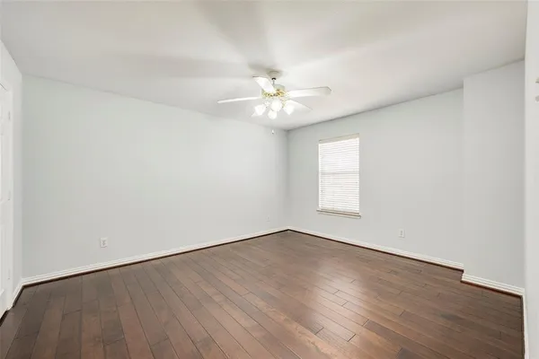 an empty room with wooden floor chandelier fan and windows