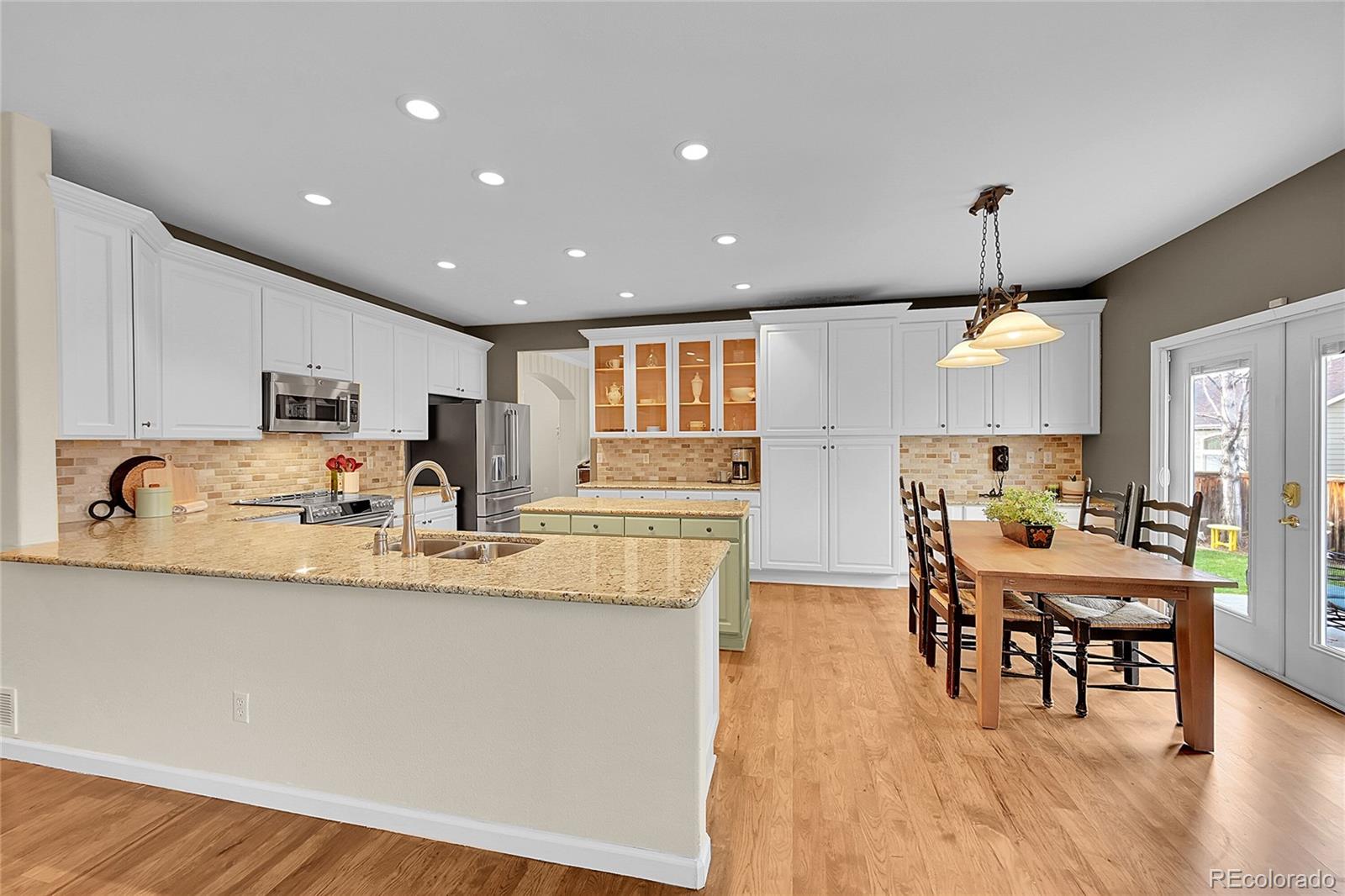 9424 South Hackberry Lane Highlands Ranch, CO 80129 - Photo 12 of 47 a large white kitchen with granite countertop a stove a sink a dining table and chairs