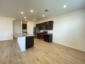 213 Saide Street Georgetown, TX 78626 - Photo 10 of 32 Open-concept kitchen featuring an island with a light-toned countertop, dark wood cabinetry, stainless steel appliances, recessed lighting, and wood-finish flooring