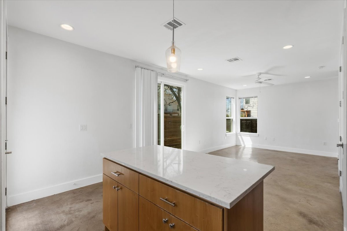 1114 Walton Lane, Unit A Austin, TX 78721 - Photo 10 of 36 Kitchen with concrete flooring, a kitchen island, wood finish cabinets, light stone counters, and pendant lighting