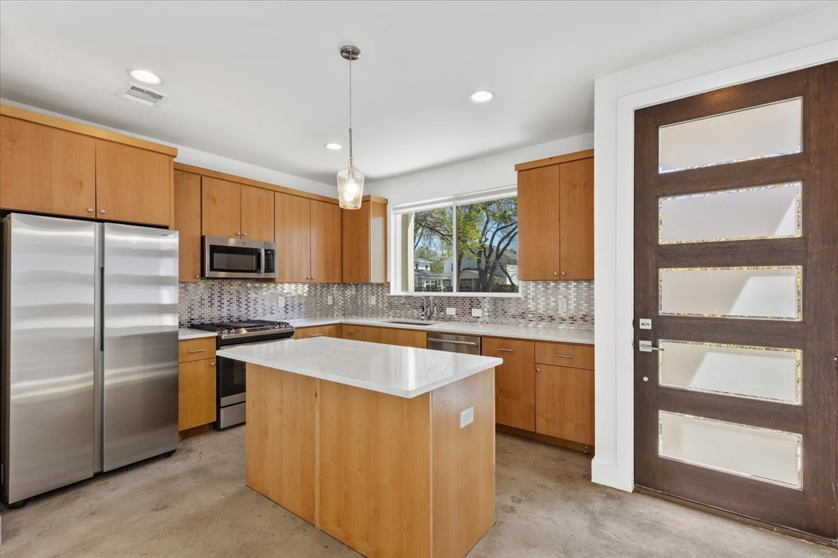 1114 Walton Lane, Unit A Austin, TX 78721 - Photo 4 of 36 Kitchen with stainless steel appliances, a center island, light stone counters, pendant lighting, and tasteful backsplash