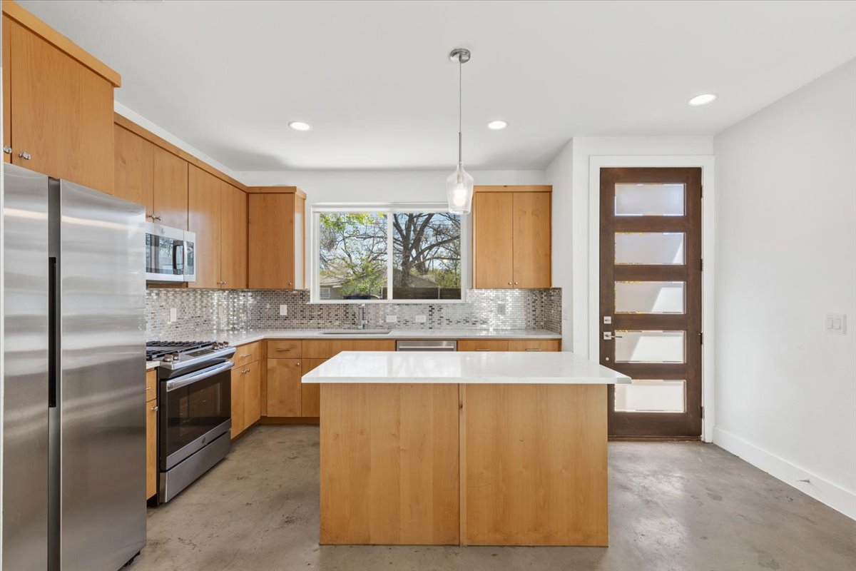 1114 Walton Lane, Unit A Austin, TX 78721 - Photo 5 of 36 Kitchen featuring stainless steel appliances, hanging light fixtures, a kitchen island, and concrete flooring