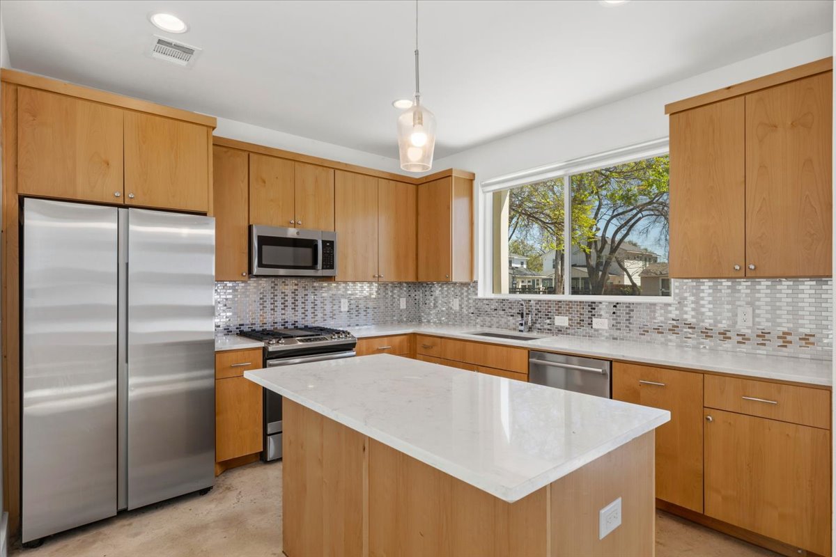 1114 Walton Lane, Unit A Austin, TX 78721 - Photo 7 of 36 Kitchen featuring stainless steel appliances, a center island, backsplash, light stone counters, and pendant lighting