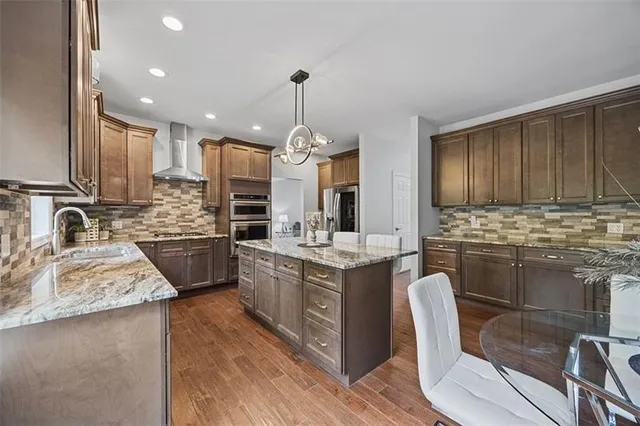 a kitchen with stainless steel appliances granite countertop wooden cabinets a sink dishwasher a stove and a refrigerator with wooden floor