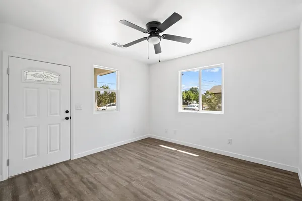 an empty room with wooden floor ceiling fan and windows