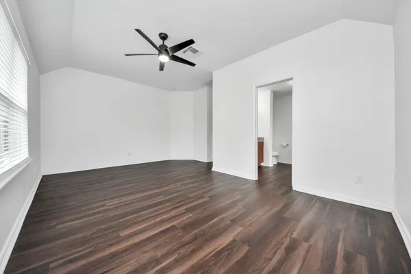 an empty room with wooden floor a ceiling fan and windows
