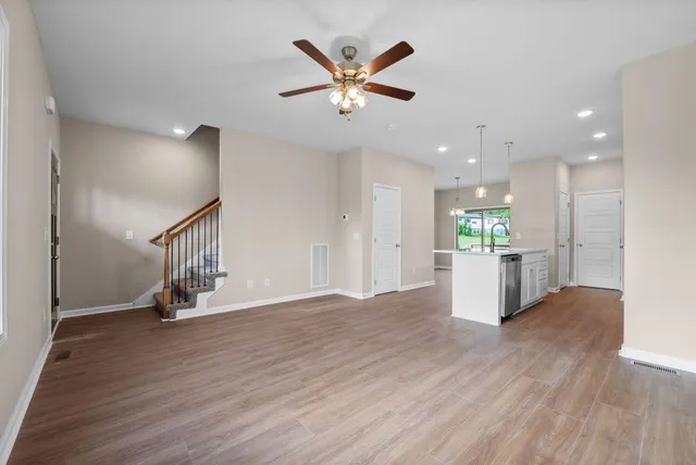 a view of an empty room with wooden floor and a ceiling fan