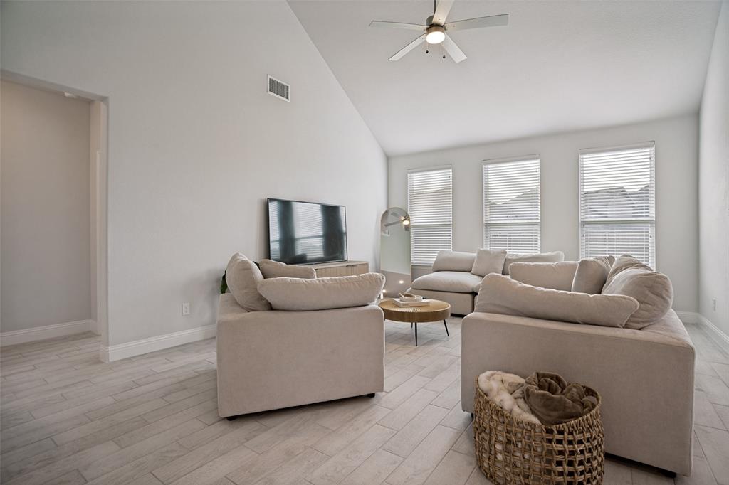 3115 Giovanni Point Princeton, TX 75407 - Photo 4 of 26 Vaulted ceiling living area featuring light wood-finish flooring, three windows with blinds, a ceiling fan with integrated lighting, and white baseboards
