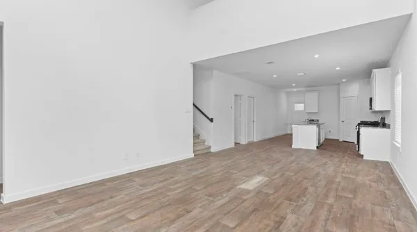 a view of an empty room with wooden floor and a kitchen